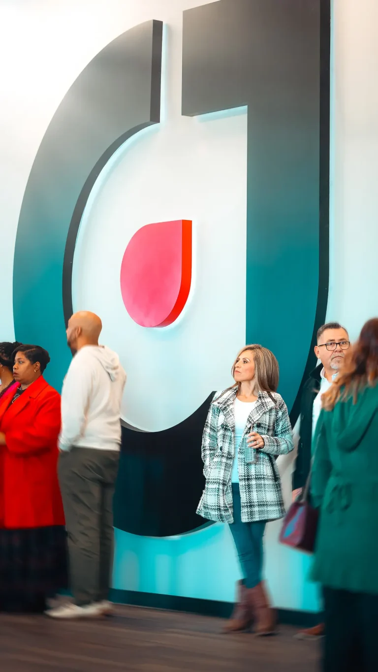 A few churchgoers standing in front of a large One City Church icon in the church lobby
