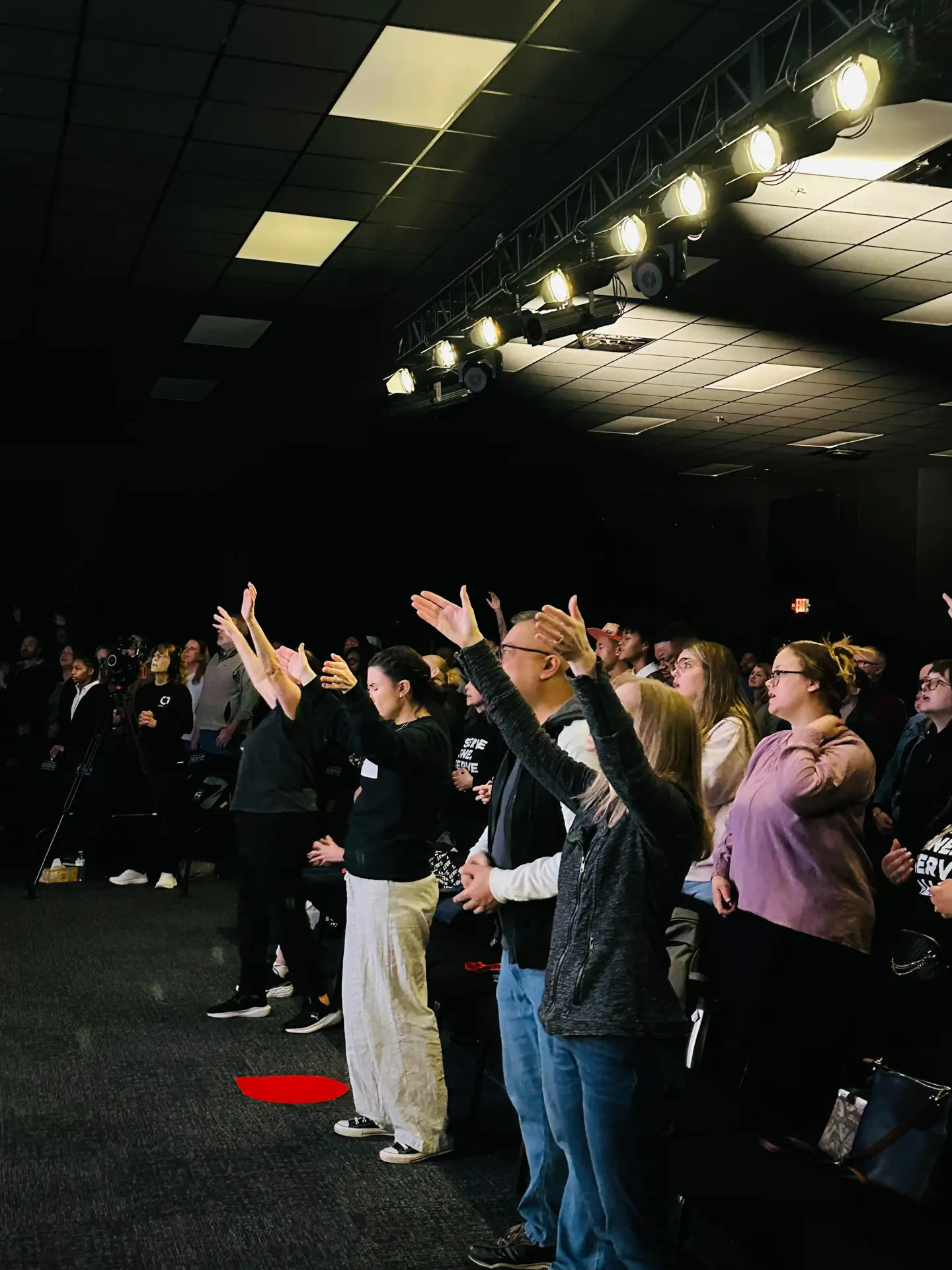 A large group of people standing and worshipping inside of a church service