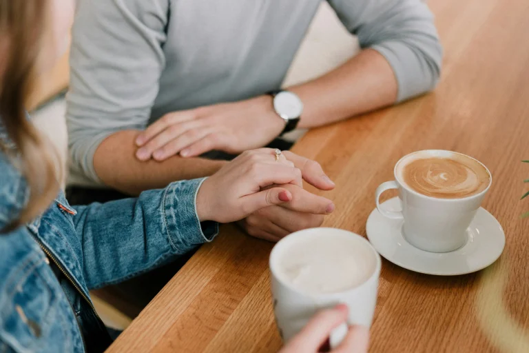 A husband and wife holding hands and talking over some coffee