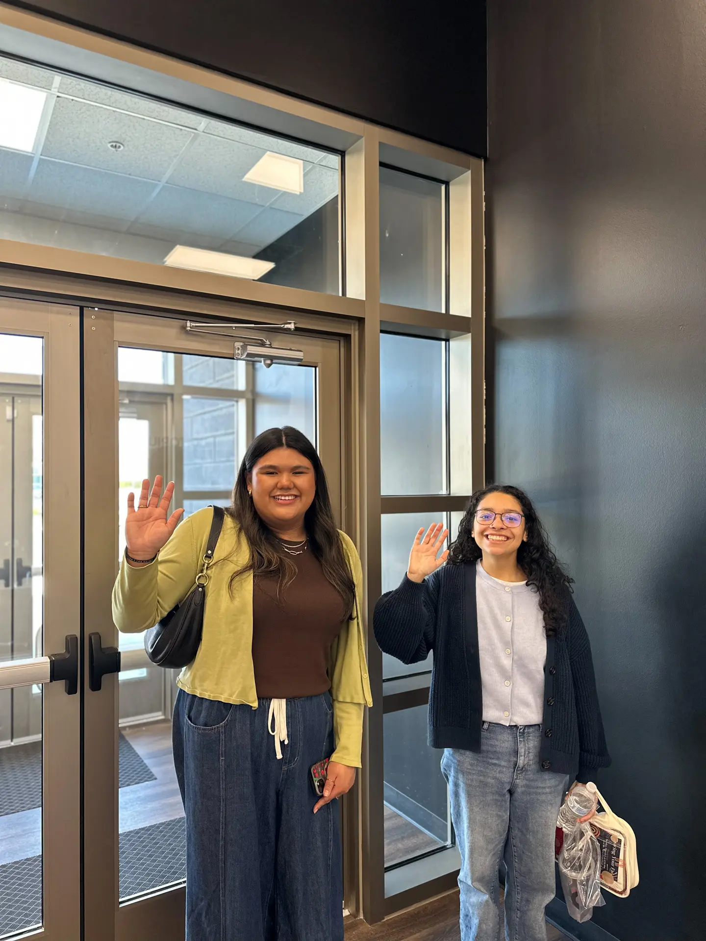 Two female students waving in front of the front doors to the church